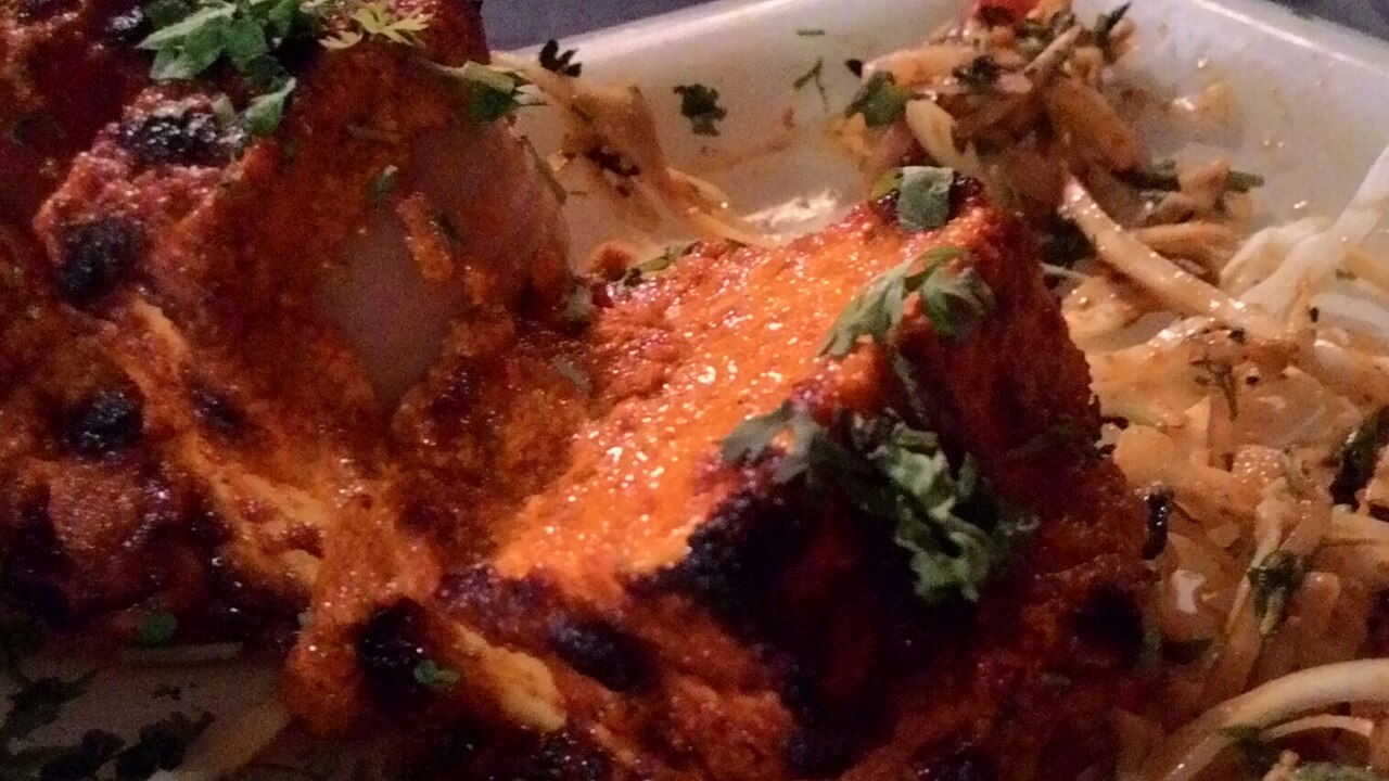Paneer tikka - tandoor-grilled paneer cubes with red-orange marinade and char marks, served with capsicum and onion